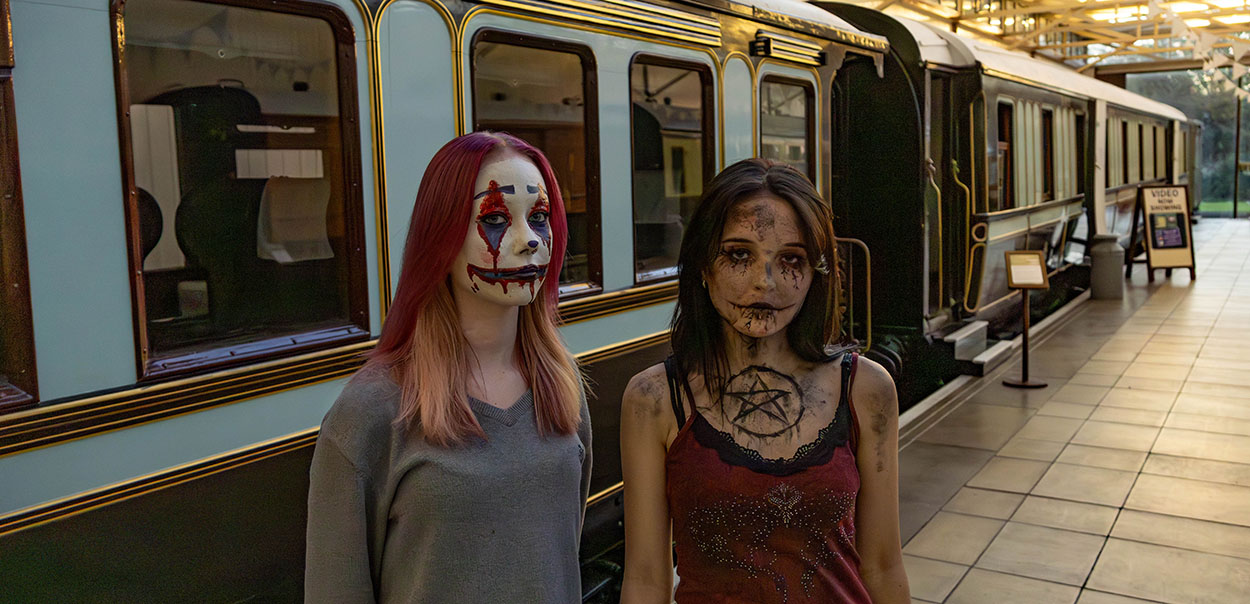 Two female actors with scary looking face makeup standing in front of a train
